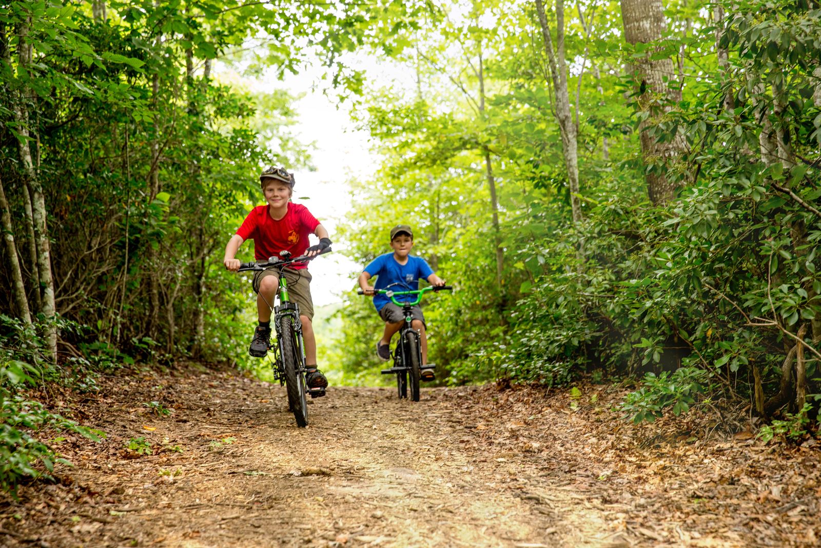 Two kids riding mountain bikes down wooded trail