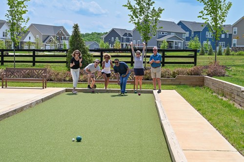 Six adults play bocce ball on an outdoor court in a suburban neighborhood.