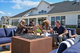 Residents enjoying drinks and conversation around a fire pit on a sunny day in Stafford, VA, with the Embrey Mill clubhouse and modern homes in the background.