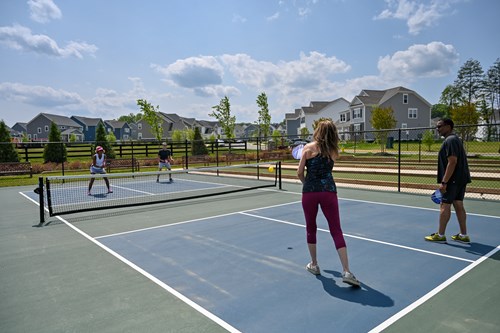 Four people playing pickleball on an outdoor court in a suburban neighborhood on a sunny day.